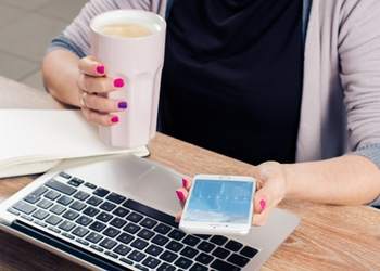 A woman is sitting at a desk with a Nexyta laptop and a cup of coffee.