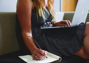 A woman using a Nexyta laptop and taking notes on a couch.