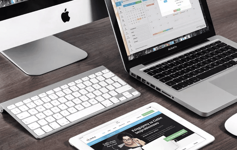 A laptop, a tablet, a phone and a keyboard on a desk.